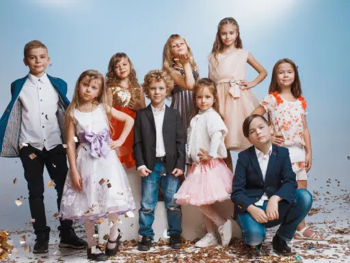 Uśmiechnięte dzieci na weselu, w eleganckich strojach, bawią się wśród konfetti.
