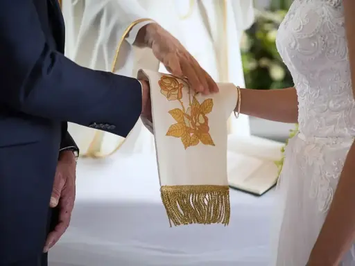 Ceremonia ślubna z kapłanem błogosławiącym ręce pary. Czy ślub kościelny ma moc prawną? To pytanie zadaje sobie wiele par.