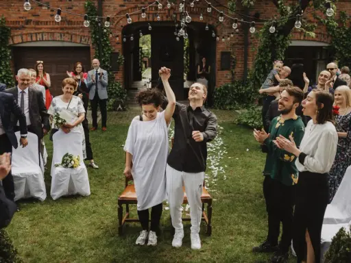Para młoda świętuje ślub cywilny na luzie, trzymając się za ręce. Goście klaszczą, ciesząc się radosnym momentem.