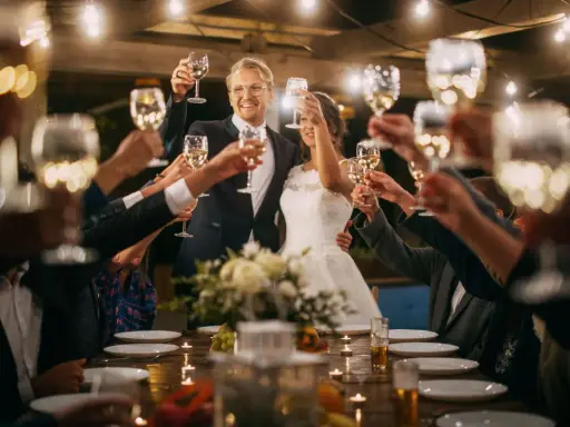 Wesele, toast wzniesiony kieliszkami. Para młoda w centrum, goście wokół stołu. Biesiada gorzka wódka tekst.