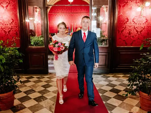 Para idzie po czerwonym dywanie, ona w białej sukni z bukietem, on w granatowym garniturze. To ich ślub rzymski.