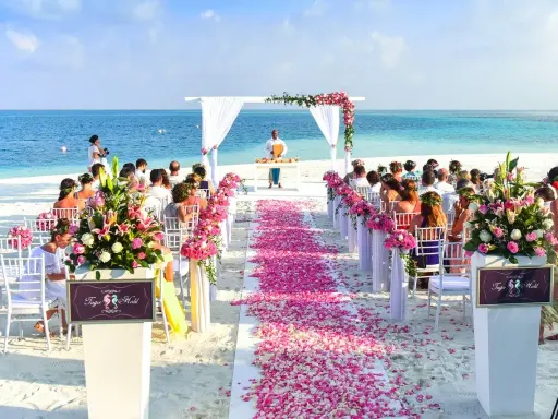 Plażowa ceremonia ślubna z różowymi płatkami kwiatów i błękitnym oceanem w tle. Idealne, nietypowe miejsce na wesele marzeń.