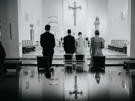 Para młoda i ksiądz podczas ślubu w kościele. W tle krzyż. W odbiciu na podłodze widać, jakby pieniądze w bucie ślubnym.
