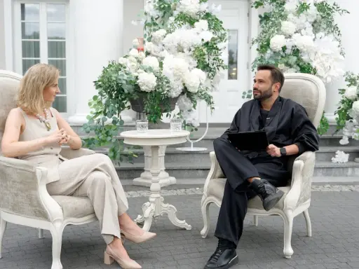 Para, która planuje filmy o weselach, siedzi w eleganckich fotelach wśród białych kwiatów.