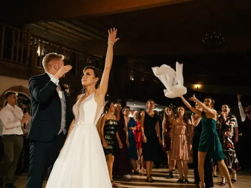 Panna młoda rzuca welonem, tradycyjny moment oczepin. Goście weselni obserwują z ekscytacją.