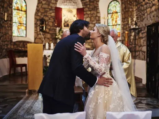 Para młoda całuje się w kościele podczas ślubu kanonicznego. Panna młoda w pięknej sukni, pan młody w garniturze.