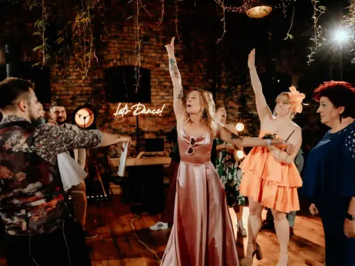 Nowoczesne oczepiny w blasku neonu "Let's Dance!". Kobiety w sukniach unoszą ręce, celebrując radosny moment.