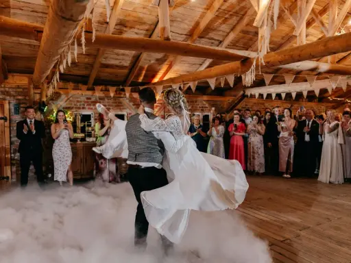 Para młoda tańczy w dymie, tworząc magiczne uroczystości weselne inaczej. Goście obserwują z zachwytem.
