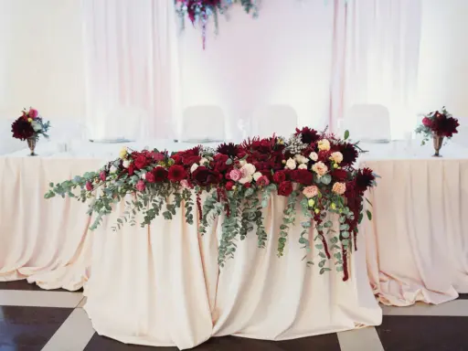 Elegancki bordowy wystrój sali weselnej z bogatą dekoracją kwiatową na stole.