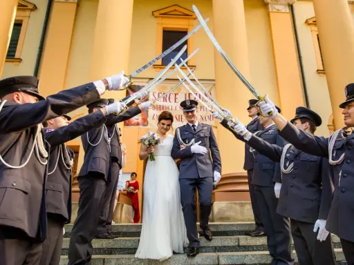 Para młoda przechodzi pod łukiem z szabel, tworząc tradycyjne wejście do kościoła ślub.