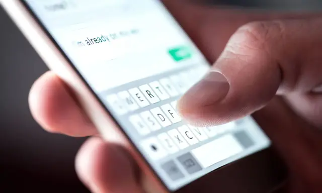 Palec pisze na klawiaturze telefonu: "Już w drodze". Potwierdzenie przybycia na wesele sms.