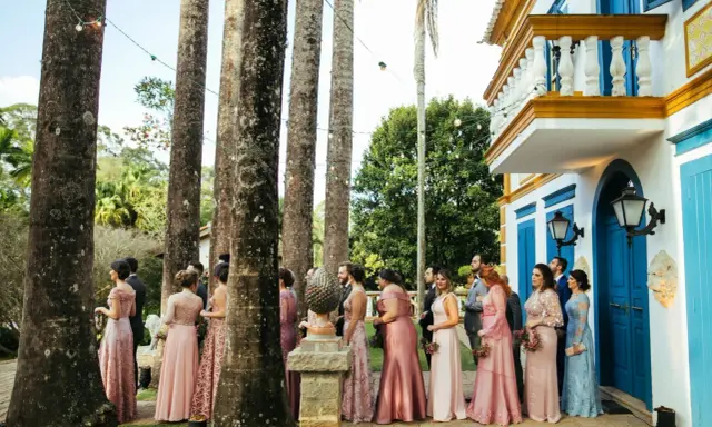 W orszaku panny młodej, panie w różowych sukniach stoją wśród palm, czekając na ceremonię.