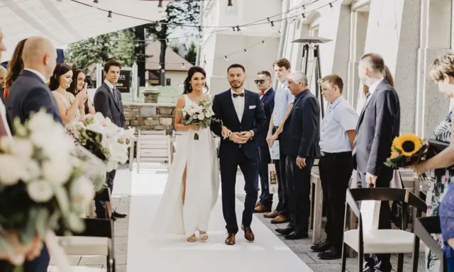 Para młoda idzie do ołtarza podczas przyjęcia po ślubie cywilnym. Panna młoda w białej sukni z bukietem kwiatów, pan młody w granatowym garniturze.