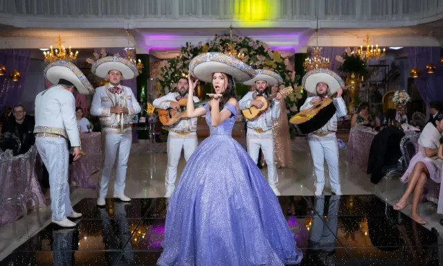 Dziewczyna w fioletowej sukni i mariachi śpiewają, tworząc atmosferę pełną radości i być może sprośnych przyśpiewek.