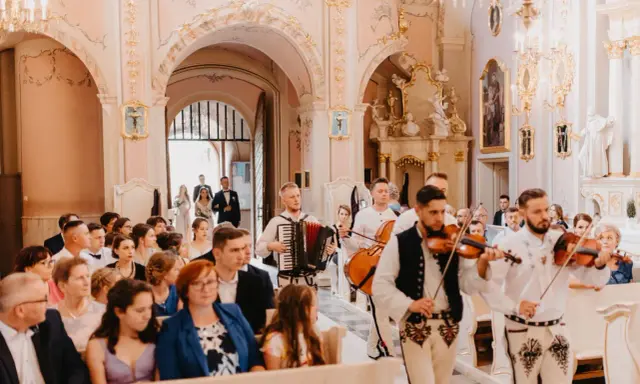 Muzycy w strojach ludowych grają tradycyjne pieśni na ślub w kościele. W tle para młoda wchodzi do świątyni.