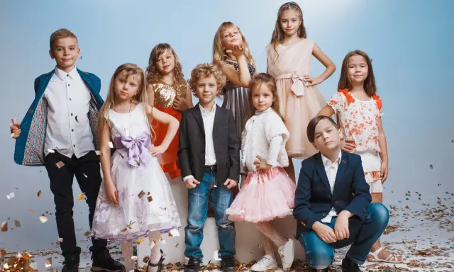Uśmiechnięte dzieci na weselu, w eleganckich strojach, bawią się wśród konfetti.