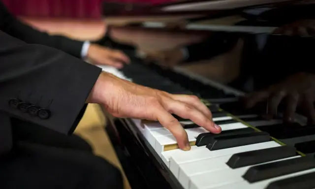 Dłoń muzyka w garniturze gra na fortepianie. Zastanawiasz się, ile bierze organista za ślub?