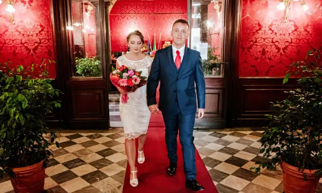 Para idzie po czerwonym dywanie, ona w białej sukni z bukietem, on w granatowym garniturze. To ich ślub rzymski.
