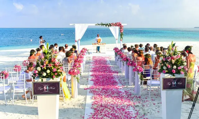 Plażowa ceremonia ślubna z różowymi płatkami kwiatów i błękitnym oceanem w tle. Idealne, nietypowe miejsce na wesele marzeń.