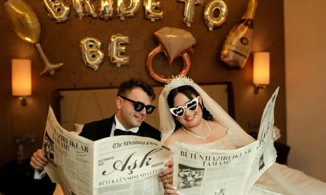 Para młoda czyta gazetę "The Wedding Post" z nagłówkami o ślubie. Czyżby to zapowiedź, ile trwają poprawiny?