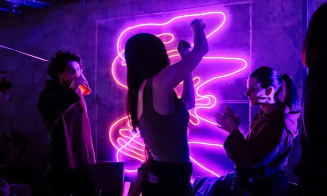 Ludzie tańczą w rytm energicznych piosenek do tańca, w otoczeniu fioletowego neonu.