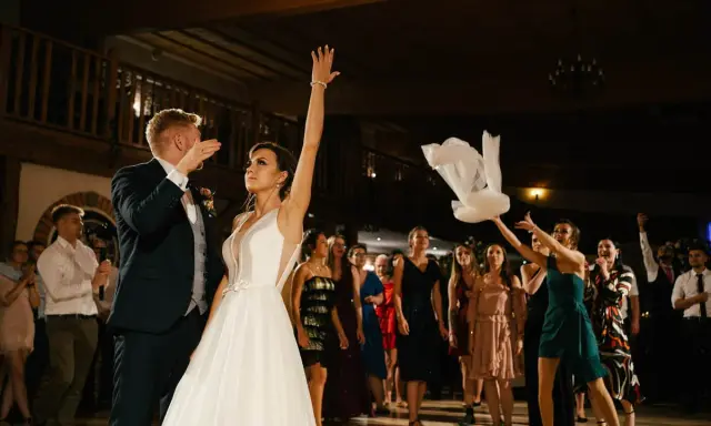 Panna młoda rzuca welonem, tradycyjny moment oczepin. Goście weselni obserwują z ekscytacją.