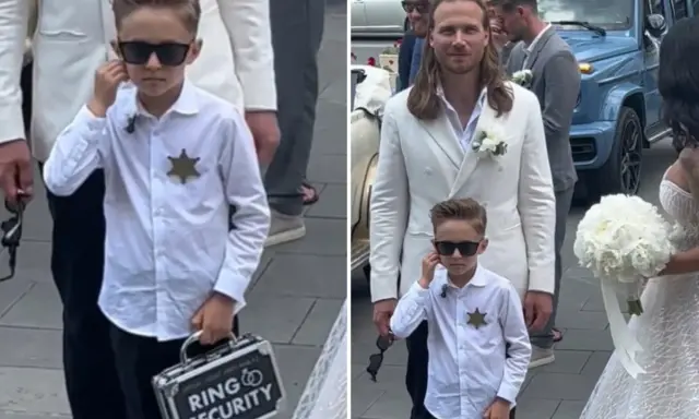 Chłopiec w okularach przeciwsłonecznych, z odznaką i walizką "Ring Security", niesie obrączki do ślubu.