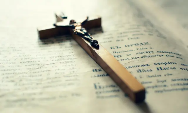Drewniany krzyż na otwartej księdze. Może symbolizować pytania małżeńskie i duchowe poszukiwania.