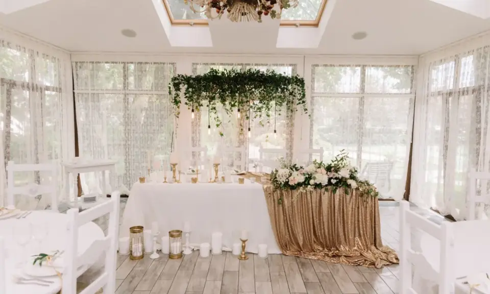 Elegancka sala weselna z białymi krzesłami i stołem pary młodej ozdobionym złotymi cekinami i kwiatami. Wspaniałe kolory na wesele.