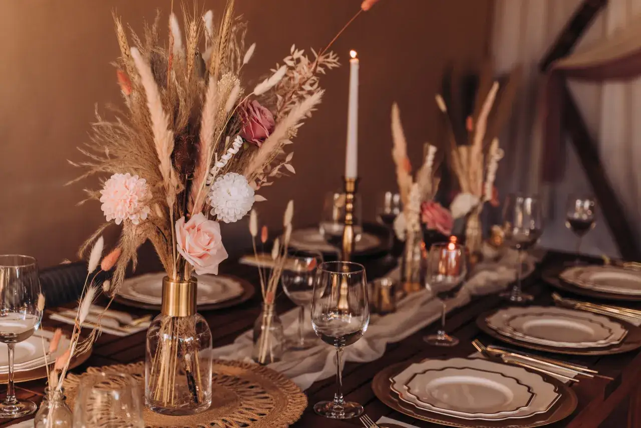 Eleganckie dekoracje stoł&oacute;w weselnych w stylu boho: bukiety z traw, r&oacute;że, świece i złote naczynia tworzą ciepłą atmosferę.