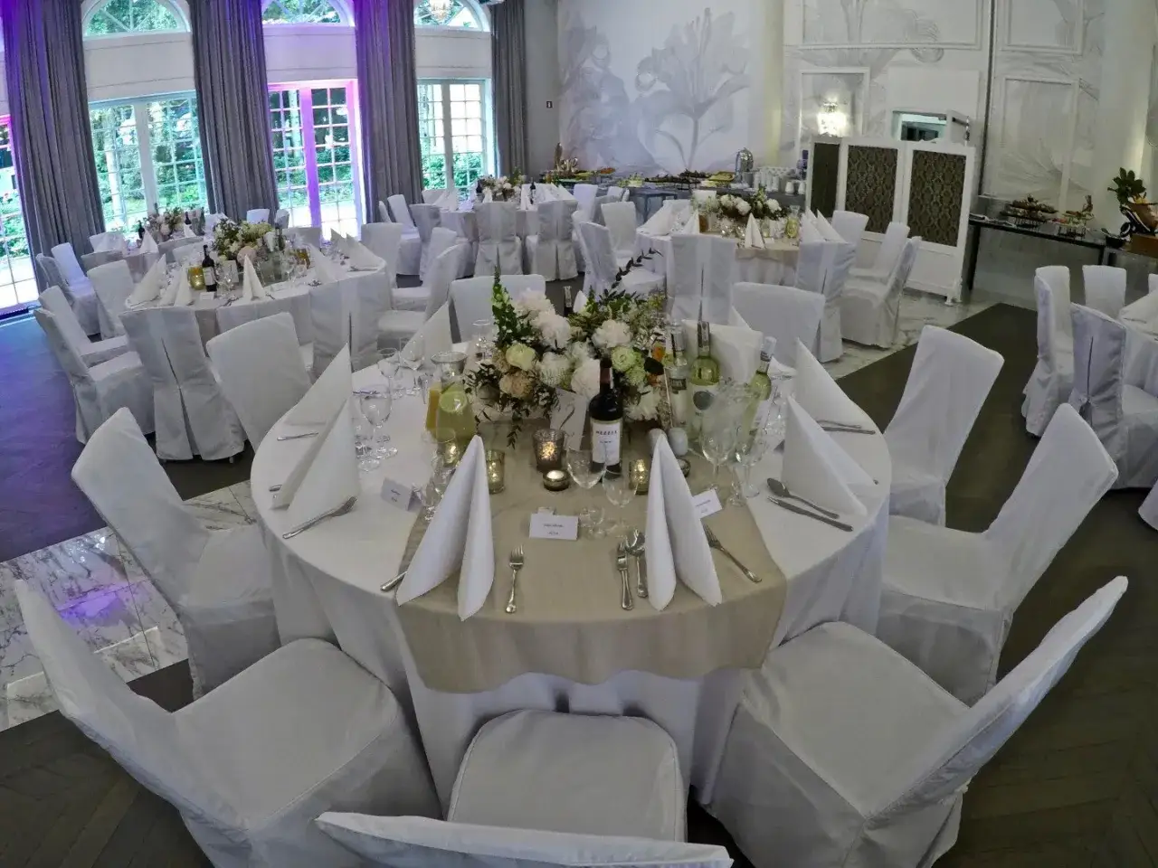 Elegancka sala weselna z białymi pokrowcami na krzesłach i udekorowanymi stołami. Zastanawiasz się, ile trwają poprawiny?