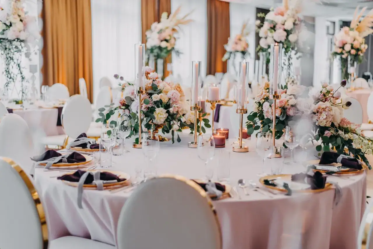 Eleganckie nakrycia stołów z pastelowymi kwiatami i złotymi świecznikami. Tanie pomysły na wesele mogą wyglądać tak pięknie!