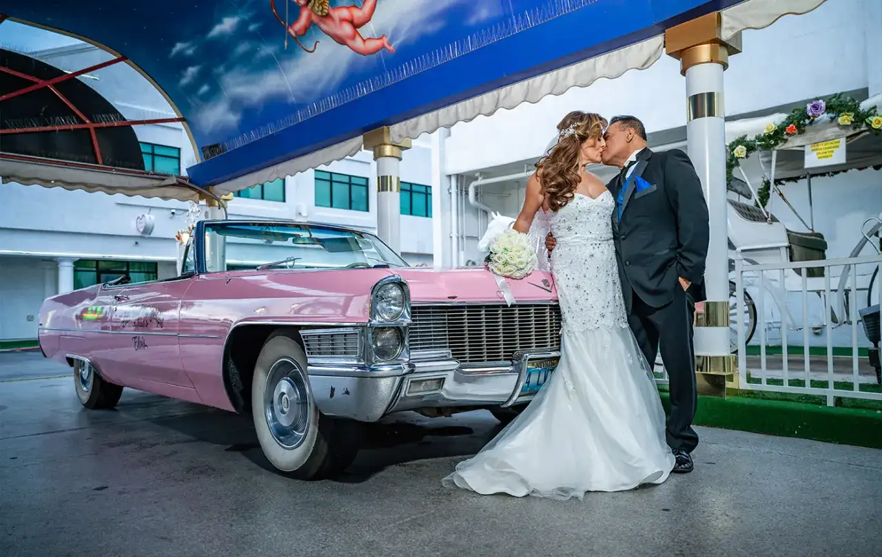 Para młoda całuje się obok różowego Cadillaca, gotowa na ślub w Las Vegas.