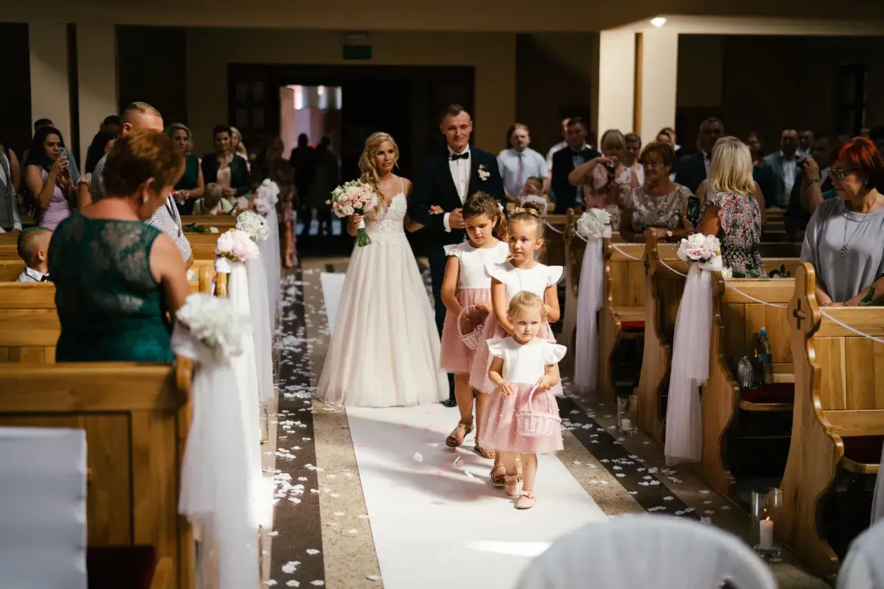 Piękna panna młoda z bukietem idzie do ołtarza w kościele ślubnym, a za nią podążają dziewczynki sypiące płatki.