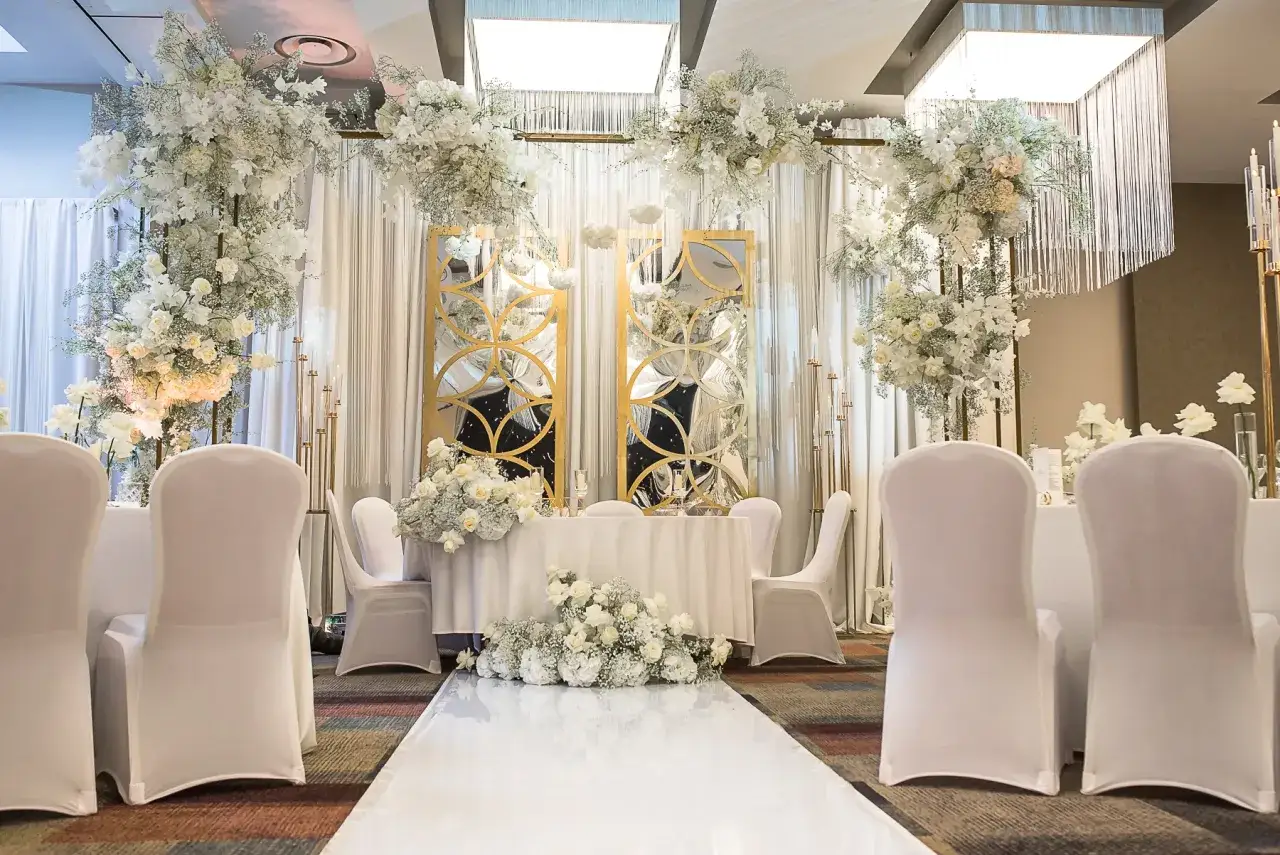Eleganckie przyjęcie po ślubie cywilnym. Białe kwiaty, złote lustra i białe pokrowce na krzesłach tworzą romantyczną atmosferę.
