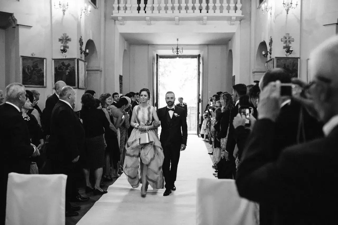 Para panny młodej idzie do ołtarza w kościele, otoczona gośćmi, którzy robią zdjęcia.