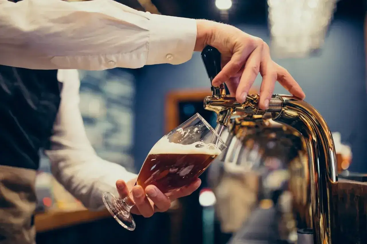 Barman nalewa piwo do kieliszka. Zastanawiasz się, ile piwa na poprawiny? To pytanie, które warto sobie zadać!