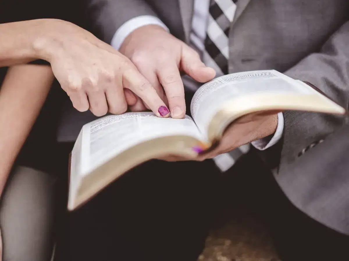 Dłonie pary wskazują na tekst w Biblii, szukając sł&oacute;w hymnu miłości.